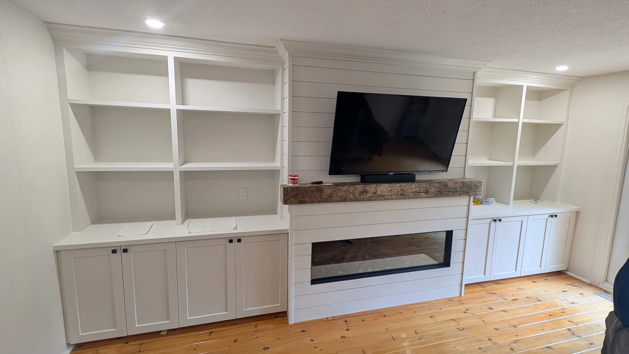 White shiplap fireplace with reclaimed wood mantel flanked by tall built-in bookshelves and cabinets