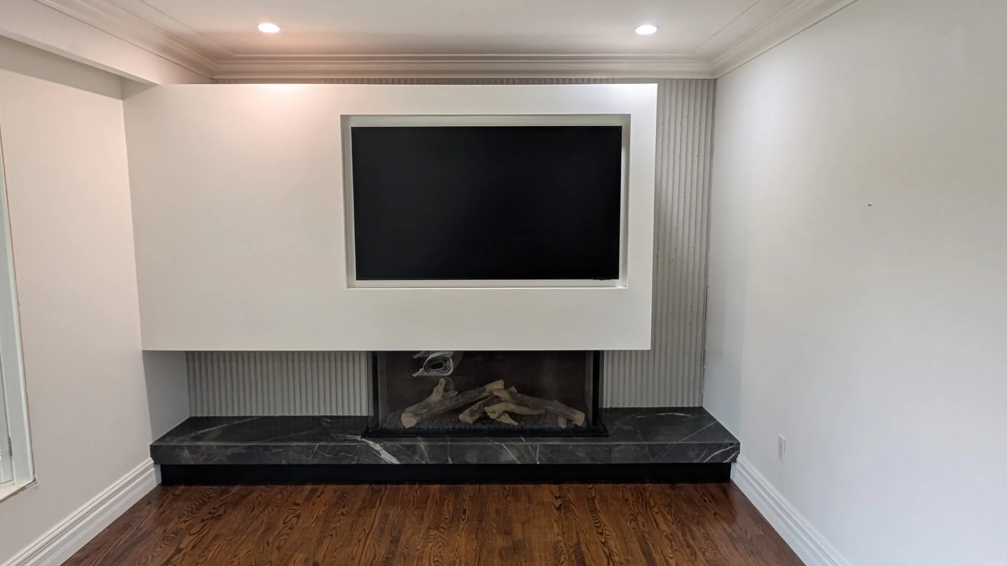Modern white plaster fireplace surround with black soapstone hearth, fluted side panels, and inset TV