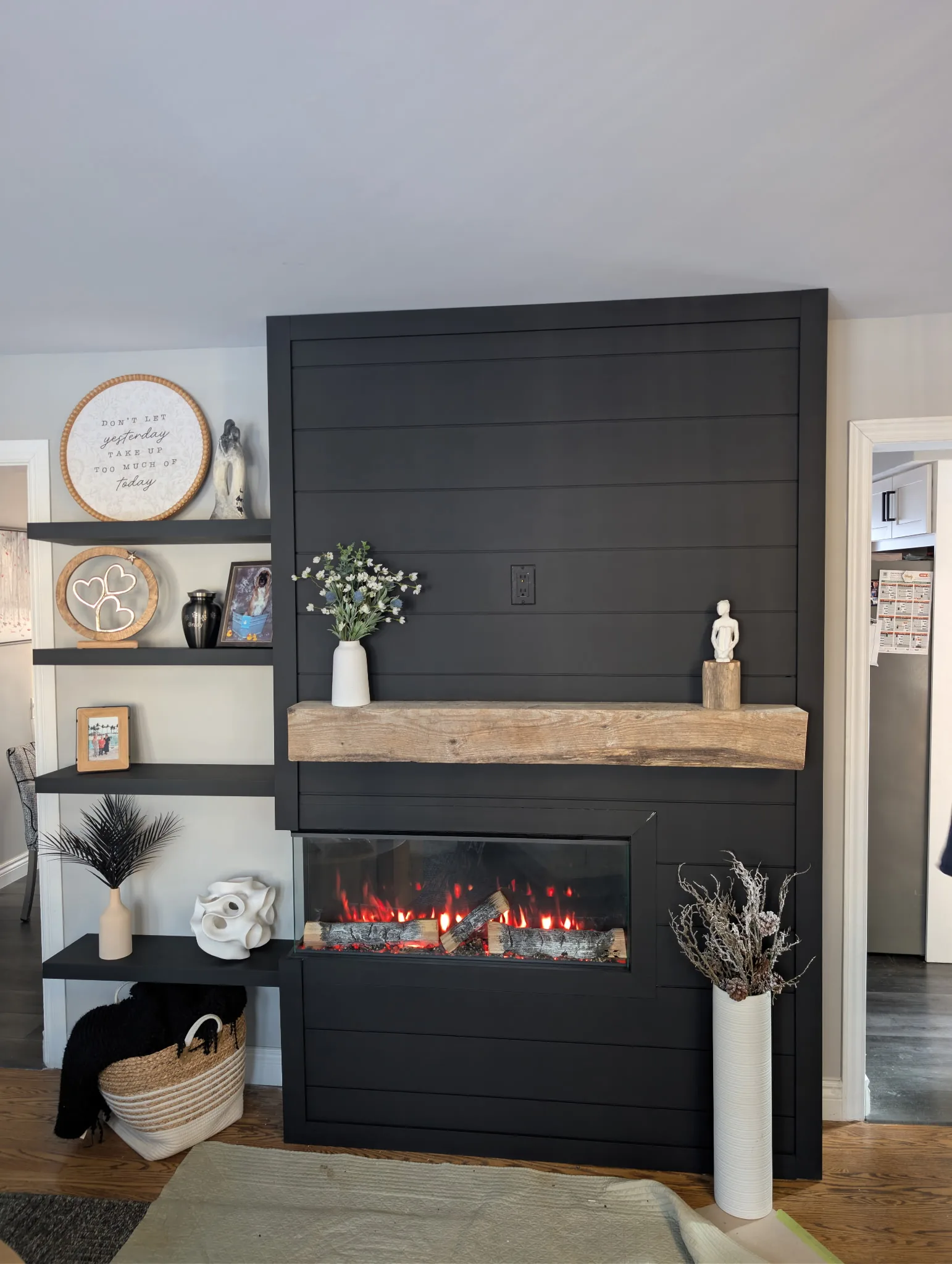 Floor-to-ceiling matte black shiplap fireplace with rustic timber mantel and glowing linear insert