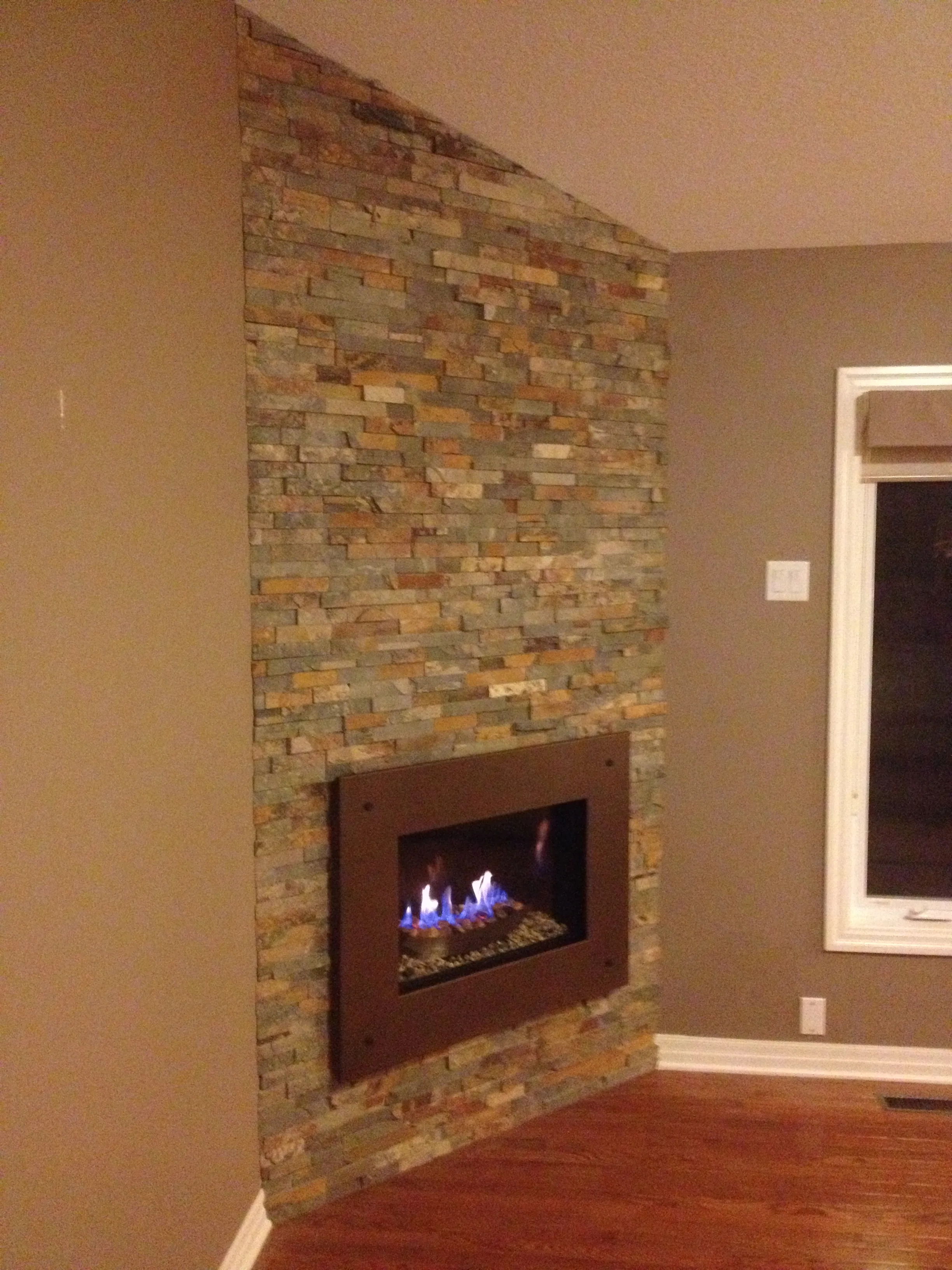 Multi-tone slate stacked-stone hearth with rectangular gas insert and adjacent wood wall