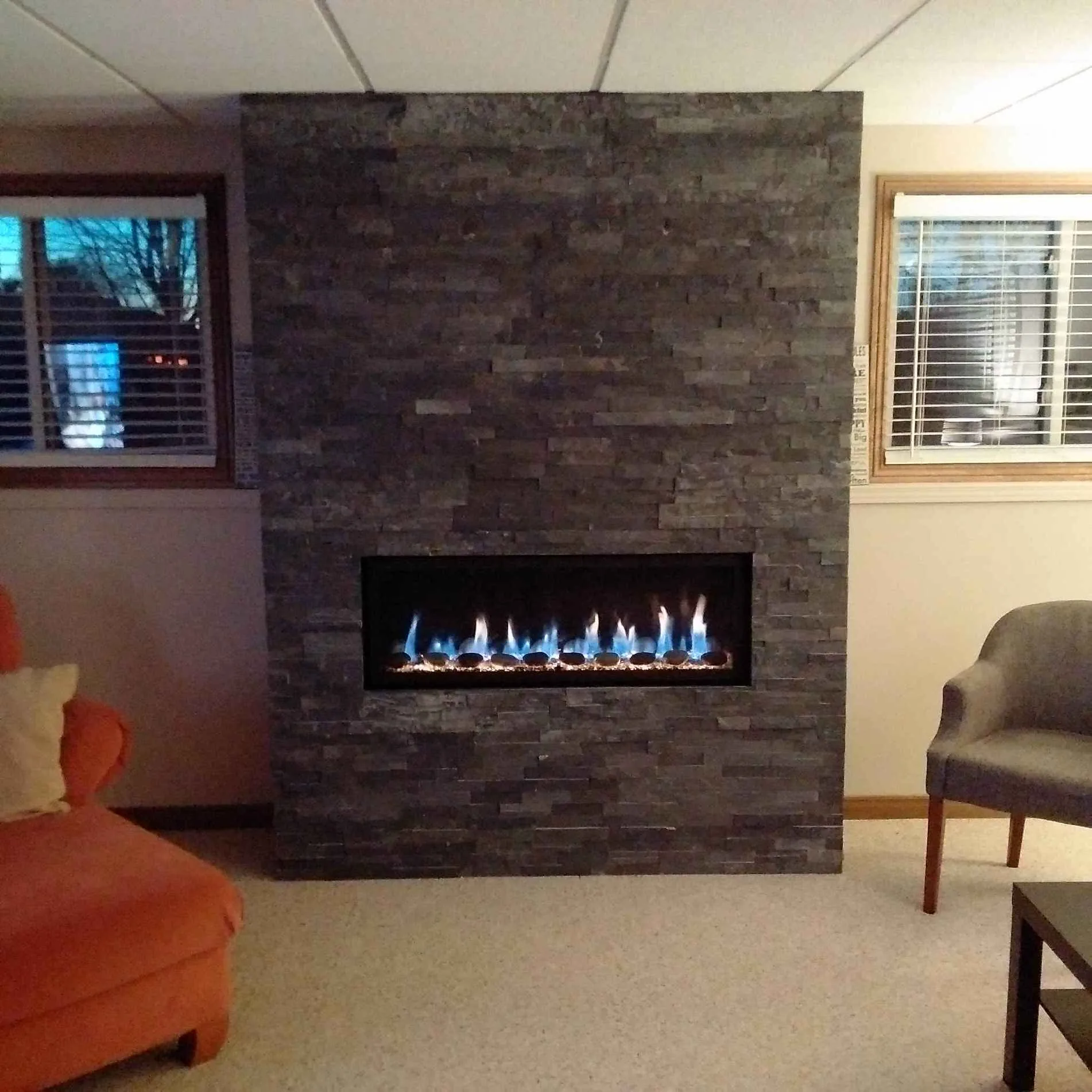 Dark grey stacked-stone accent wall with linear gas fireplace between two windows