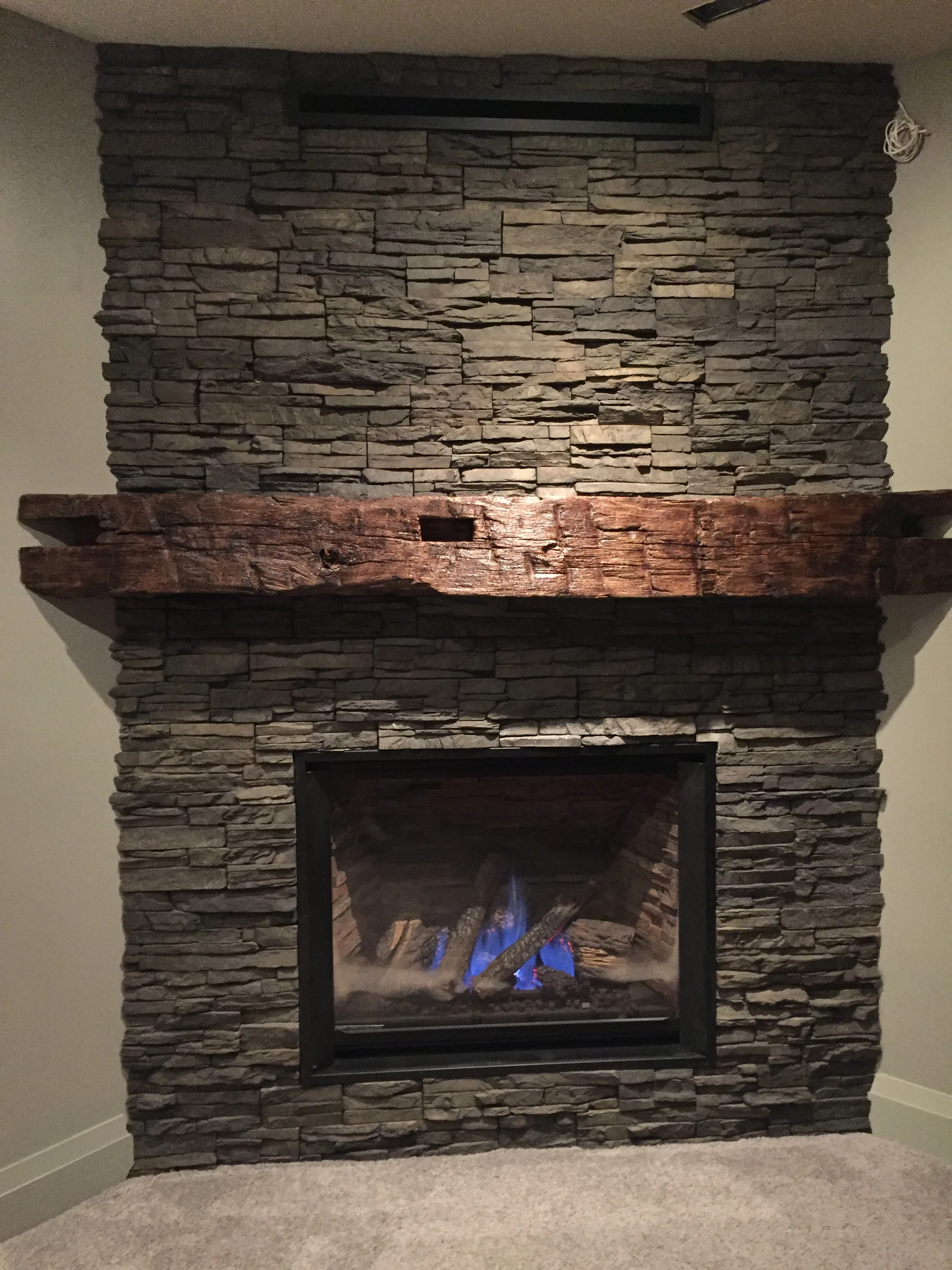 Grey ledger-stone fireplace with reclaimed timber post detail and linear insert