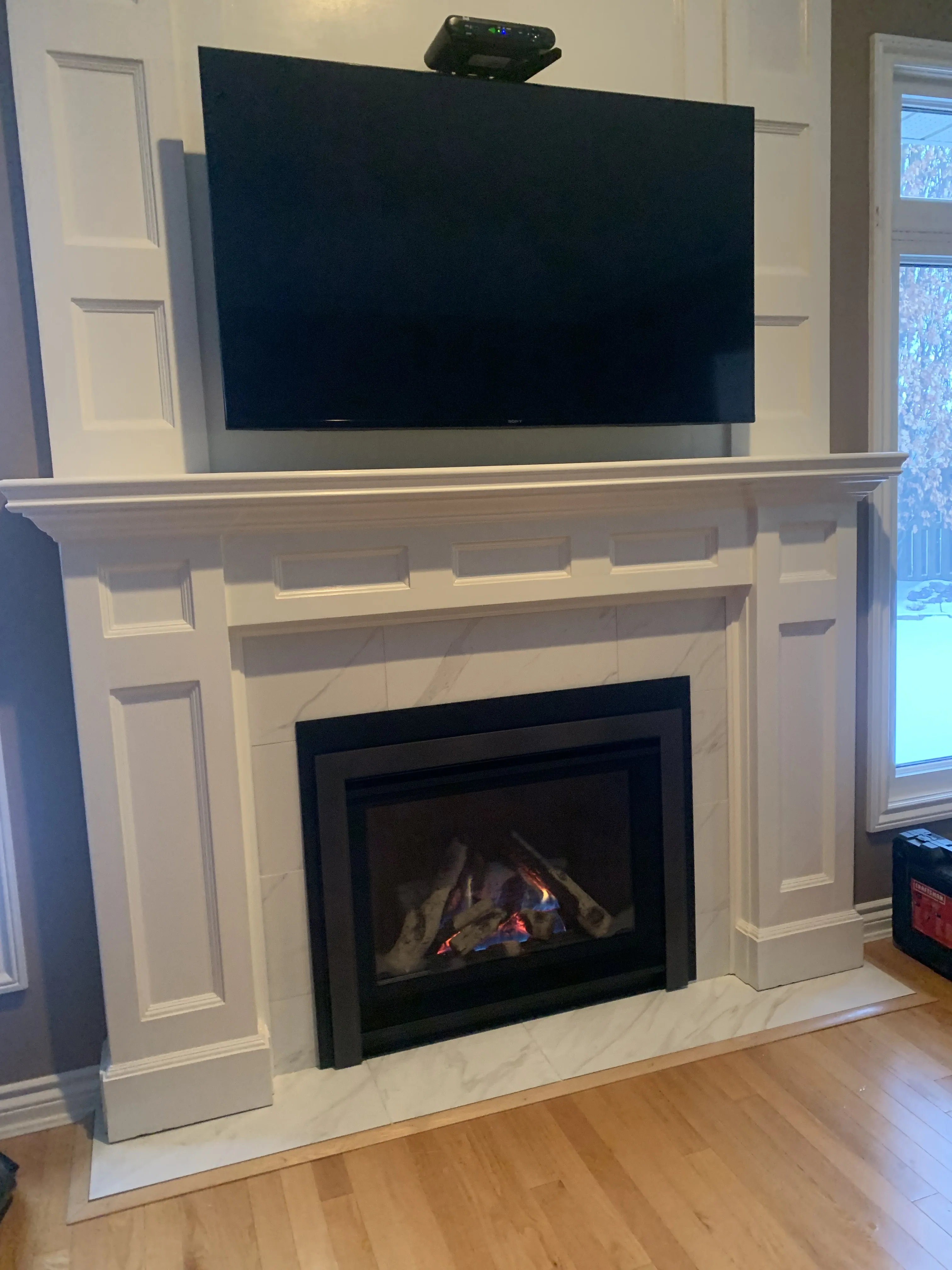 Detailed white raised-panel mantel with marble surround, dark insert, and mounted TV