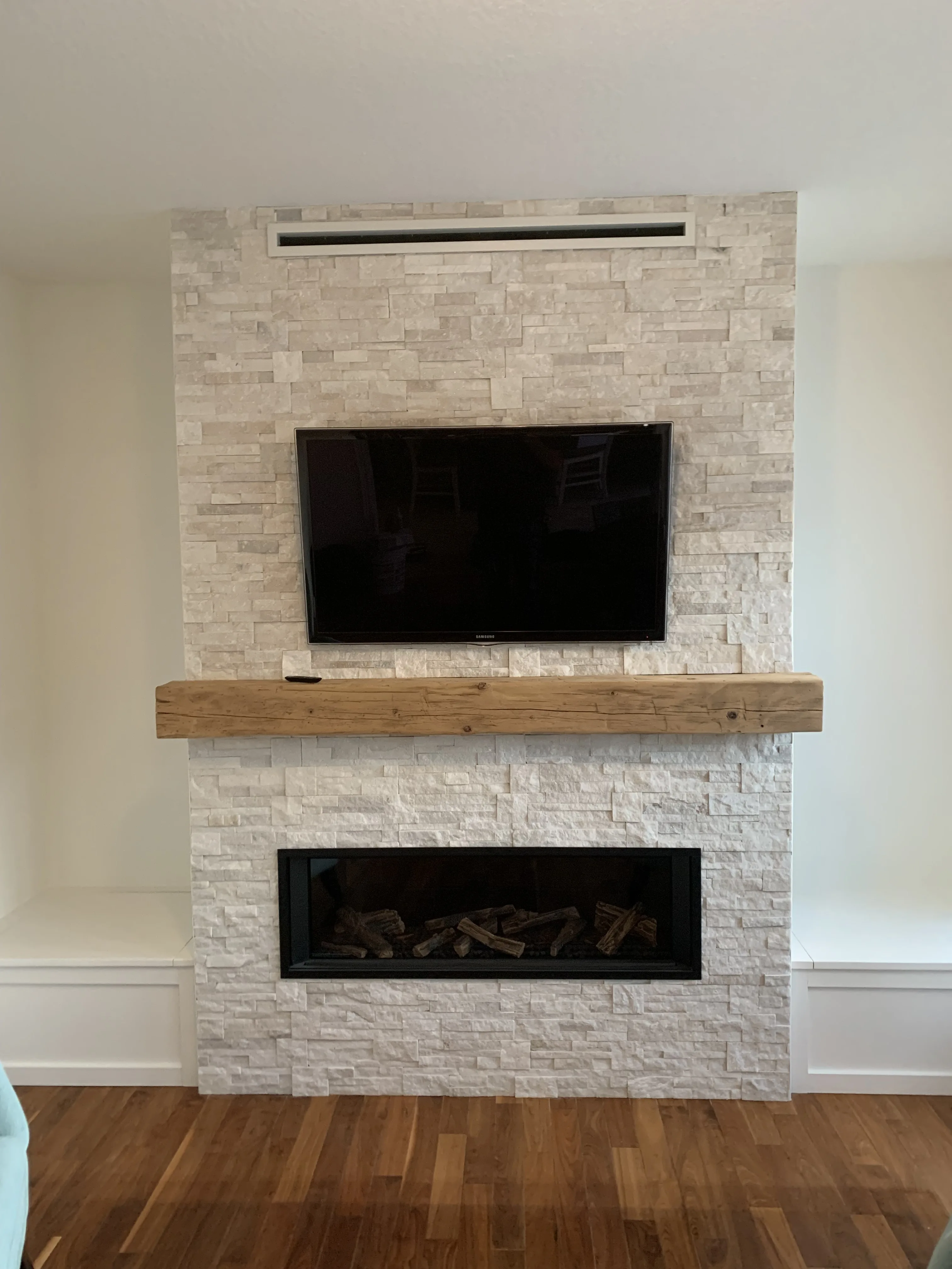 White stacked-stone fireplace with reclaimed wood mantel, twin insets, and TV niche