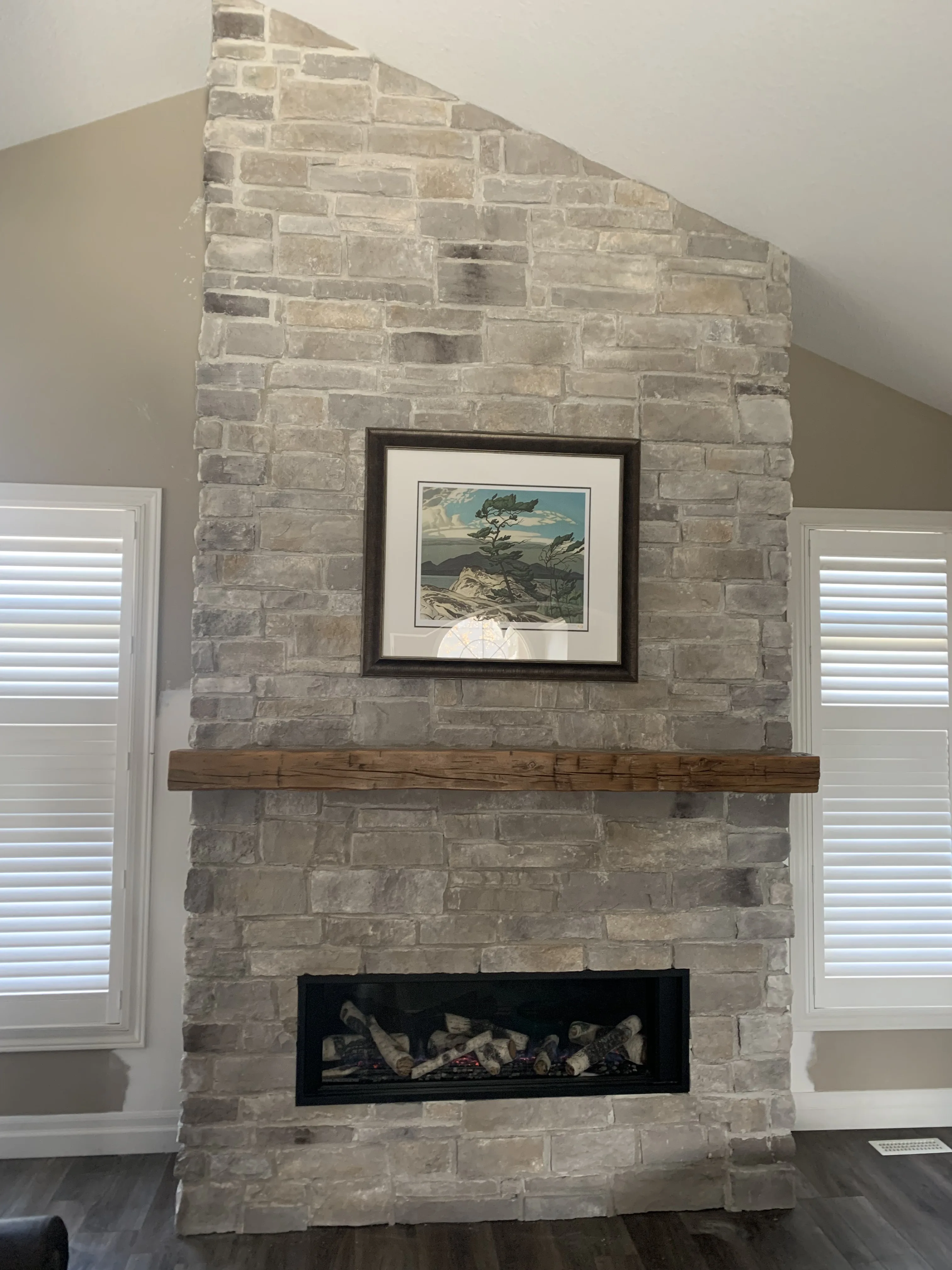 Grey ledger-stone chimney breast with reclaimed wood mantel and framed art between windows