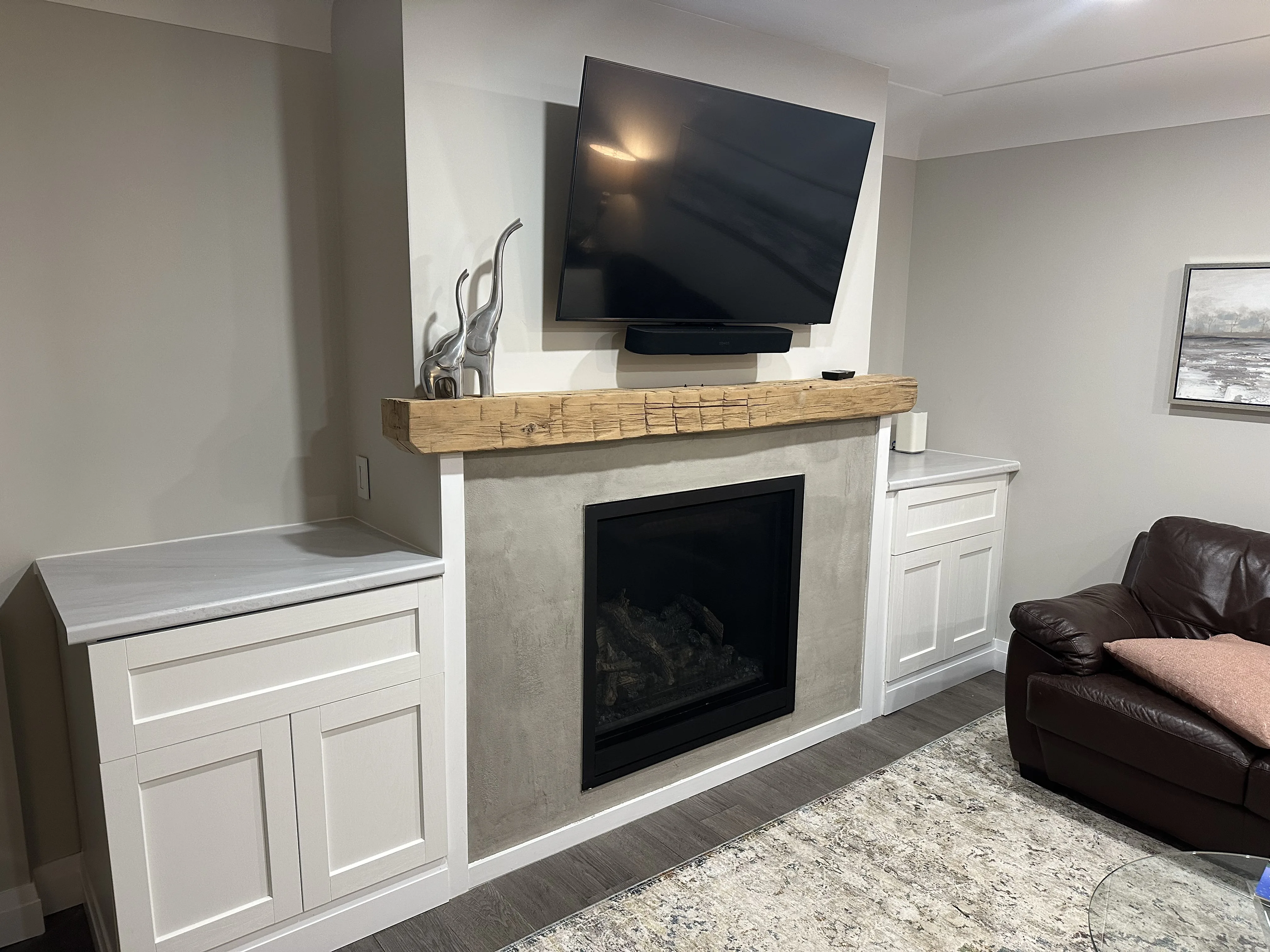 Concrete-look fireplace with rustic wood mantel, white shaker cabinets, and mounted TV