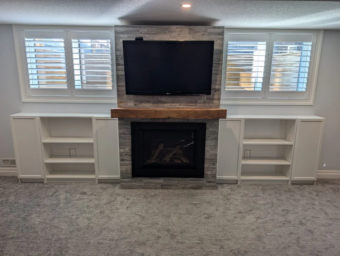 Grey stone-tile fireplace with reclaimed timber mantel, TV niche, and flanking white shutter windows