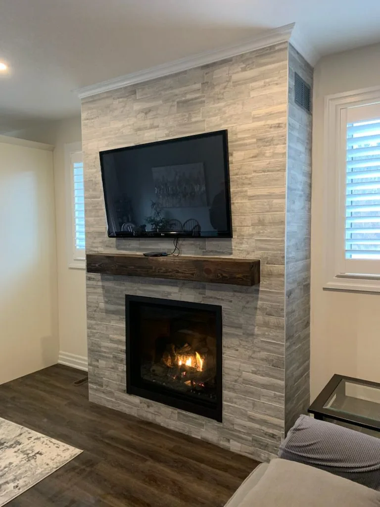 Grey stacked-stone fireplace with dark wood mantel and mounted TV in bright living room